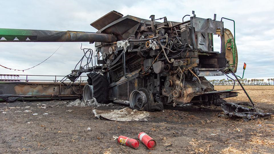 Photo of a combine harvester with burn damage due to a fire, and 2 red fire extinguishers in the foreground.